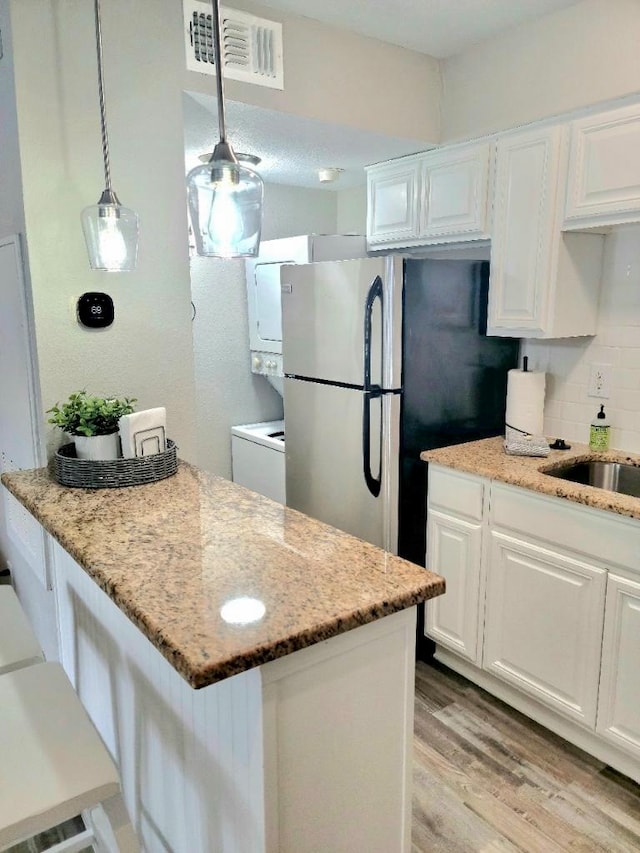 kitchen featuring white cabinets, stainless steel refrigerator, light hardwood / wood-style flooring, and light stone counters