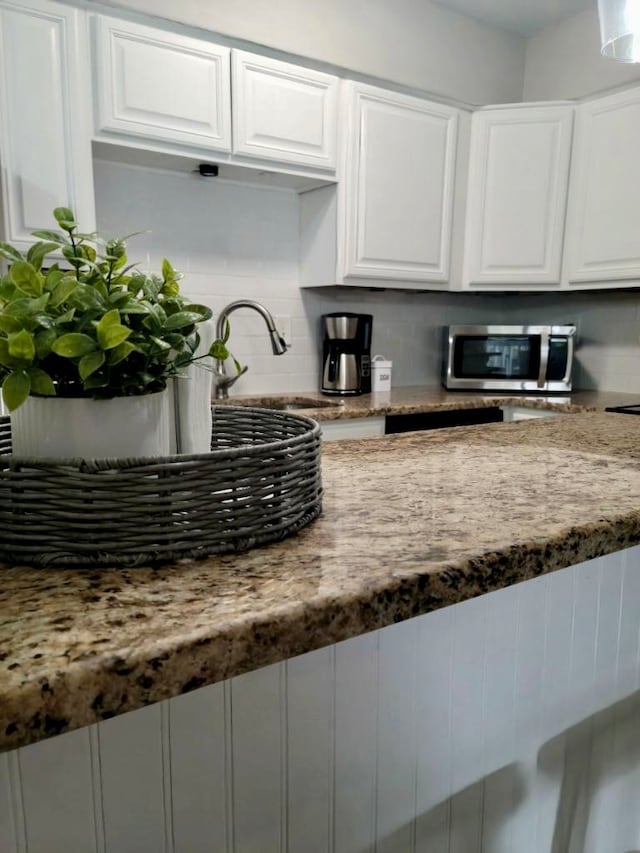 kitchen featuring white cabinets, stone counters, sink, and decorative backsplash