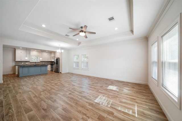 unfurnished living room with sink, light hardwood / wood-style flooring, a tray ceiling, and ceiling fan with notable chandelier