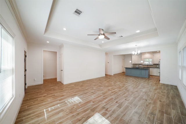 unfurnished living room featuring a raised ceiling, ornamental molding, and light wood-type flooring