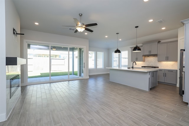 kitchen featuring pendant lighting, light wood-type flooring, an island with sink, and gray cabinetry