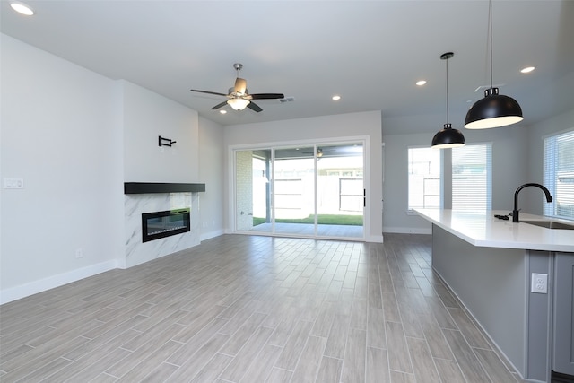 unfurnished living room featuring ceiling fan, a premium fireplace, sink, and light wood-type flooring