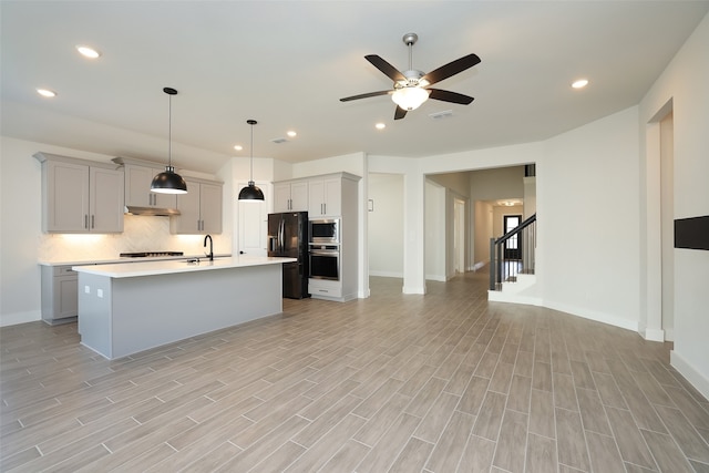 kitchen featuring a kitchen island with sink, light hardwood / wood-style flooring, stainless steel appliances, pendant lighting, and gray cabinets