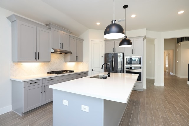 kitchen with sink, hanging light fixtures, light hardwood / wood-style floors, stainless steel appliances, and a center island with sink