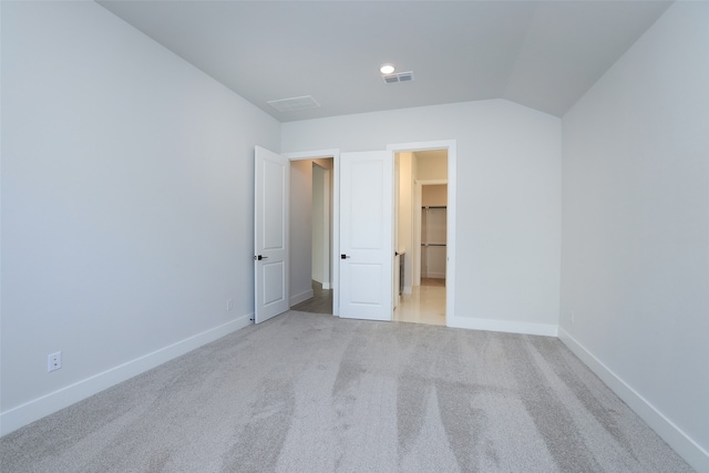 unfurnished bedroom with a spacious closet, vaulted ceiling, and light carpet