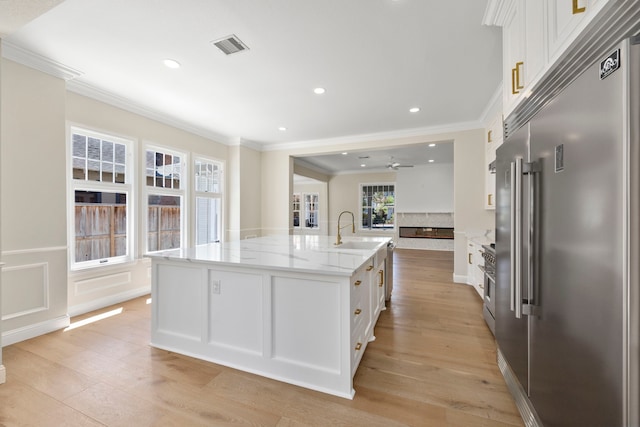 kitchen featuring stainless steel built in fridge, a large island with sink, light hardwood / wood-style flooring, and white cabinets