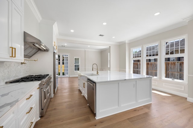 kitchen with white cabinets, an island with sink, light hardwood / wood-style flooring, stainless steel appliances, and ventilation hood