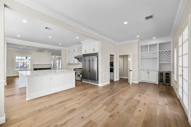 kitchen with white cabinets, tasteful backsplash, light hardwood / wood-style floors, crown molding, and premium appliances