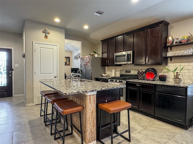 kitchen with a center island with sink, light stone counters, a breakfast bar, stainless steel appliances, and sink