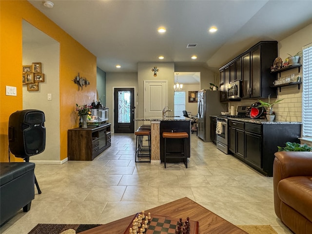 kitchen with tasteful backsplash, light stone countertops, a kitchen bar, stainless steel appliances, and a kitchen island with sink