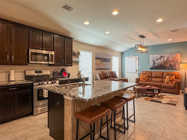 kitchen with stone counters, an island with sink, a kitchen breakfast bar, stainless steel appliances, and lofted ceiling