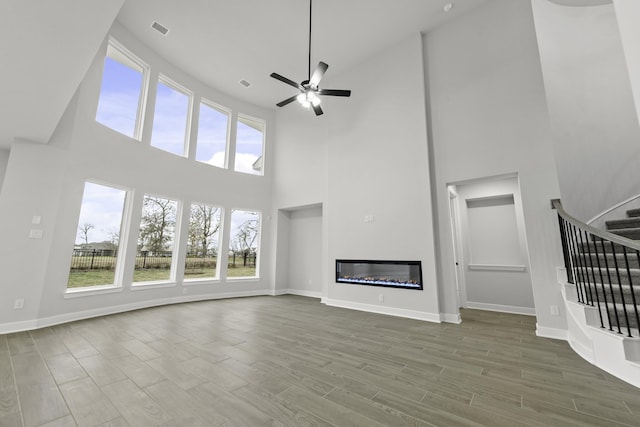 unfurnished living room with stairs, ceiling fan, visible vents, and wood finished floors