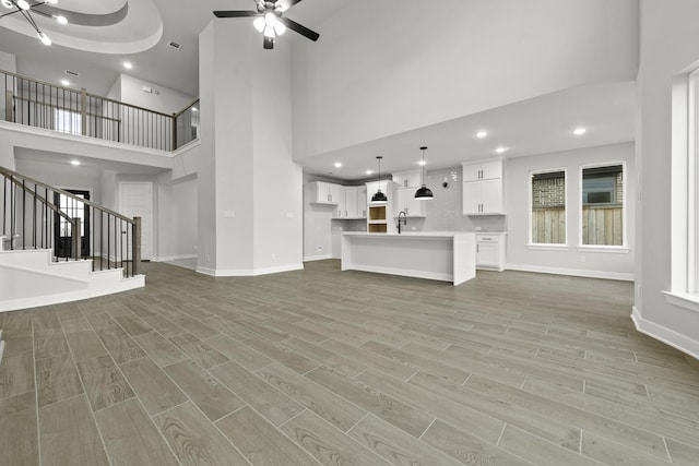 unfurnished living room with stairs, light wood-style floors, and ceiling fan with notable chandelier