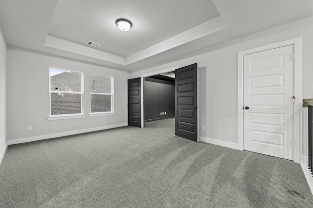 unfurnished bedroom featuring baseboards, carpet floors, a tray ceiling, and visible vents