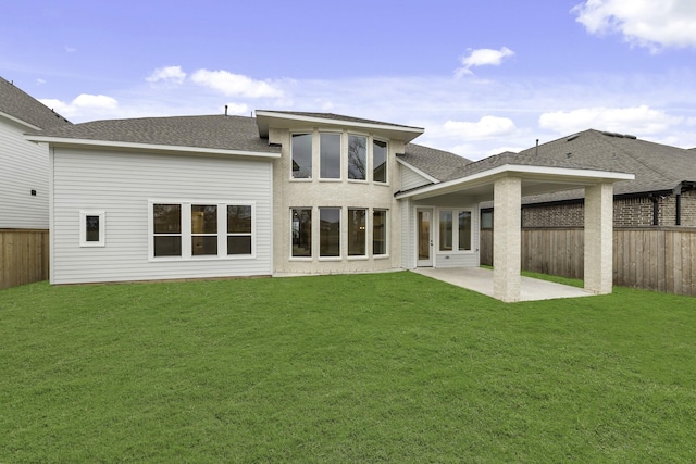 rear view of house with a fenced backyard, a lawn, a patio area, and roof with shingles