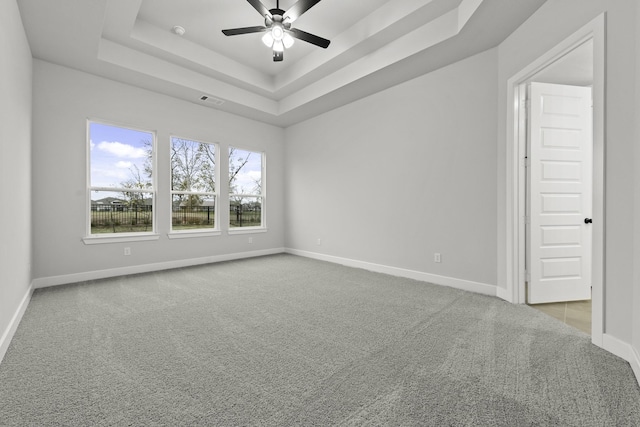 carpeted spare room with baseboards, a tray ceiling, visible vents, and ceiling fan