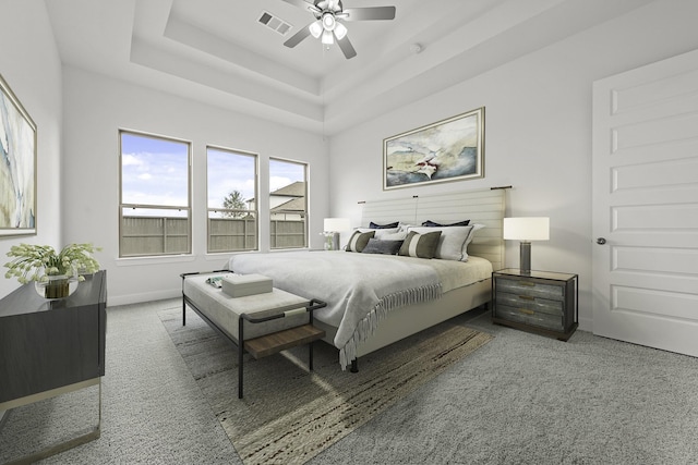 carpeted bedroom with a tray ceiling, baseboards, visible vents, and ceiling fan