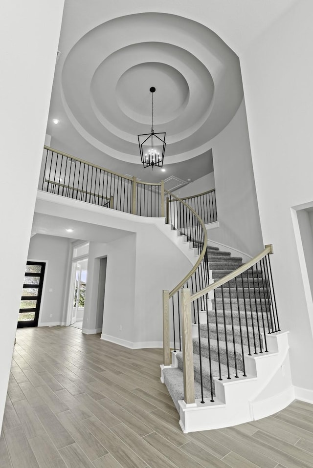 stairway featuring a notable chandelier, a raised ceiling, baseboards, wood tiled floor, and a towering ceiling
