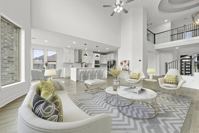 living room featuring a high ceiling, stairs, light wood-style flooring, and a ceiling fan