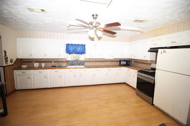 kitchen with white refrigerator, white cabinetry, a textured ceiling, and stainless steel gas stove