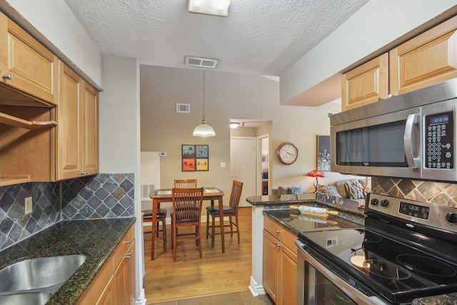 kitchen featuring light hardwood / wood-style flooring, stainless steel appliances, a textured ceiling, and dark stone counters