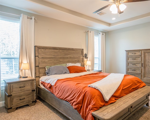 carpeted bedroom with ceiling fan and a raised ceiling