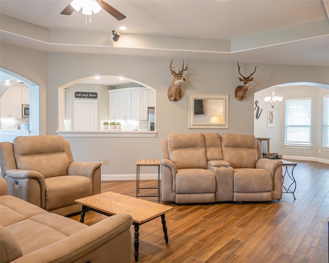 living room featuring hardwood / wood-style floors, a raised ceiling, and ceiling fan with notable chandelier