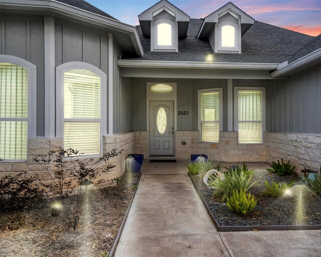 2523 Turberry Dr, West Columbia, TX 77486 - exterior entry at dusk featuring board and batten siding, a shingled roof, and stone siding