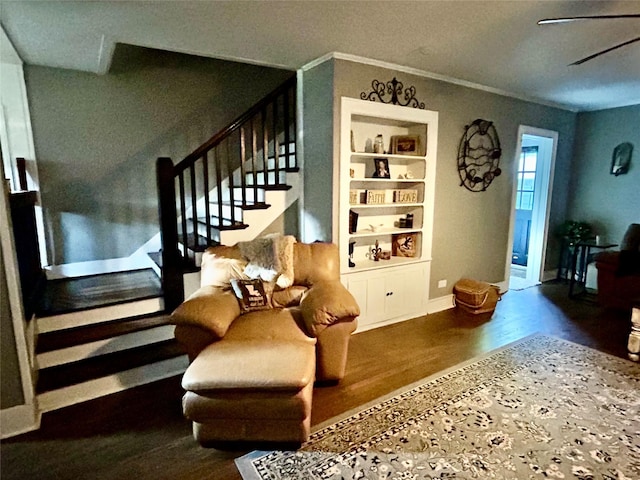 sitting room featuring built in shelves, stairs, baseboards, wood finished floors, and ornamental molding