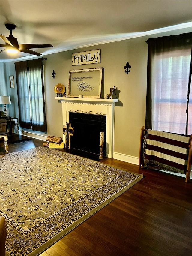 living area with a ceiling fan, crown molding, a fireplace with flush hearth, wood finished floors, and baseboards