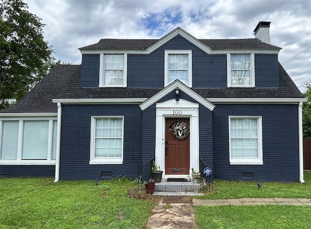 view of front facade with a shingled roof, a front lawn, brick siding, crawl space, and a chimney