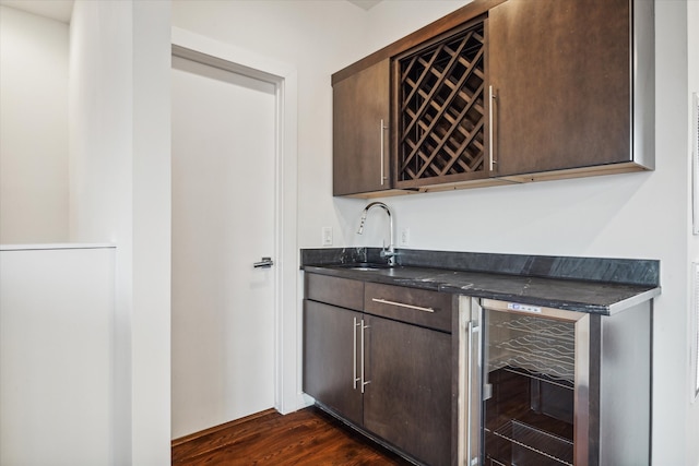 bar featuring dark brown cabinetry, beverage cooler, dark wood-type flooring, and sink