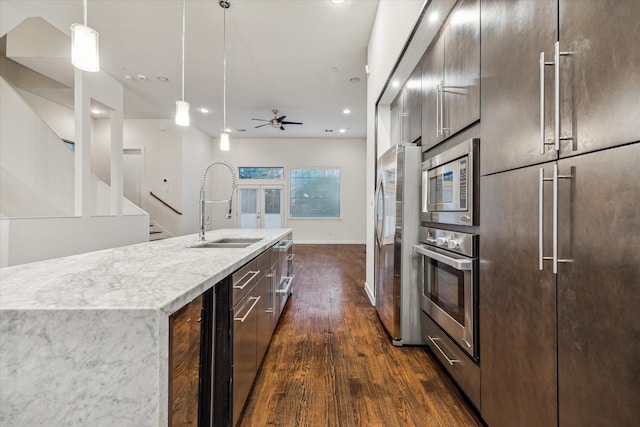 kitchen with stainless steel appliances, ceiling fan, dark wood-type flooring, sink, and a center island with sink