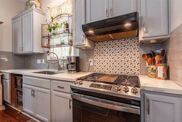 kitchen featuring dark wood-type flooring, stainless steel gas range, sink, light stone countertops, and tasteful backsplash