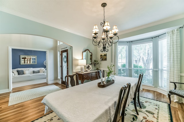 dining space with crown molding, an inviting chandelier, and light wood-type flooring