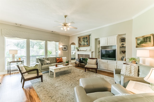 living room featuring a fireplace, crown molding, built in shelves, light hardwood / wood-style floors, and ceiling fan