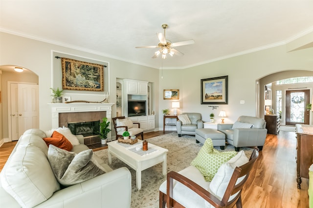 living room with a tile fireplace, crown molding, light hardwood / wood-style floors, and ceiling fan