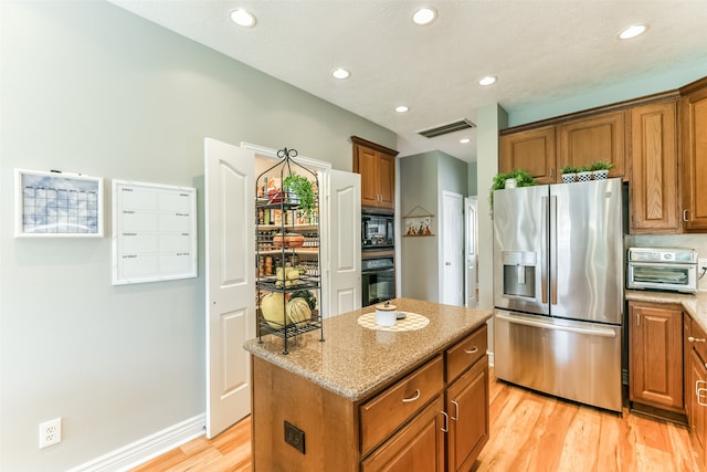 kitchen featuring light stone countertops, black appliances, a kitchen island, a textured ceiling, and light hardwood / wood-style floors