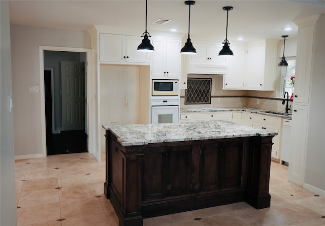 kitchen featuring a kitchen island, sink, pendant lighting, white cabinets, and white appliances