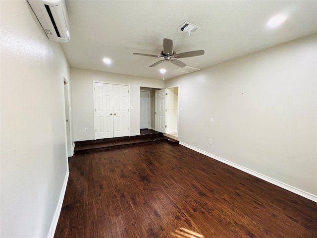 unfurnished bedroom with a wall mounted air conditioner, wood-type flooring, and ceiling fan