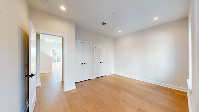 unfurnished bedroom with light wood-type flooring and multiple closets