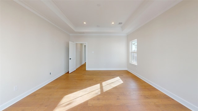 empty room featuring a raised ceiling, light wood-type flooring, and crown molding