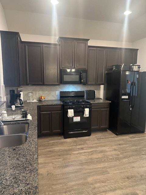 kitchen with dark brown cabinets, backsplash, dark stone countertops, black appliances, and light hardwood / wood-style floors