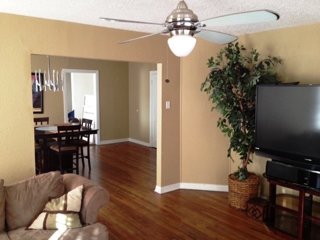 living room with dark wood-type flooring, a textured ceiling, and ceiling fan