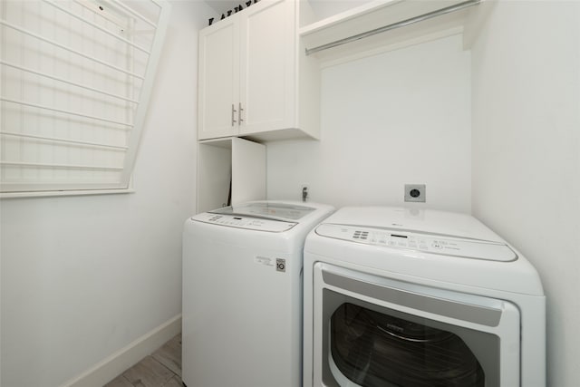 clothes washing area featuring hardwood / wood-style flooring, cabinets, and washing machine and clothes dryer