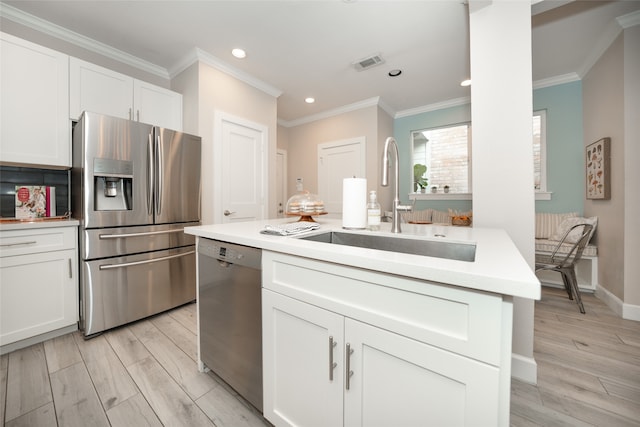 kitchen with appliances with stainless steel finishes, sink, light wood-type flooring, white cabinets, and crown molding