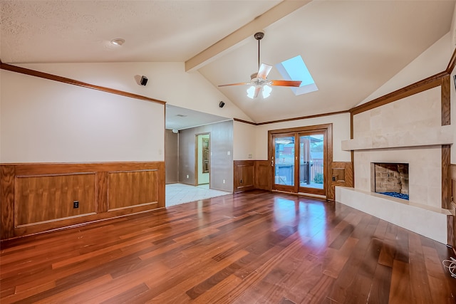 unfurnished living room with vaulted ceiling with skylight, a textured ceiling, a tile fireplace, and hardwood / wood-style floors