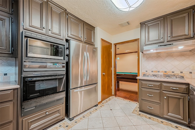 kitchen featuring backsplash, a textured ceiling, custom range hood, light tile patterned flooring, and stainless steel appliances