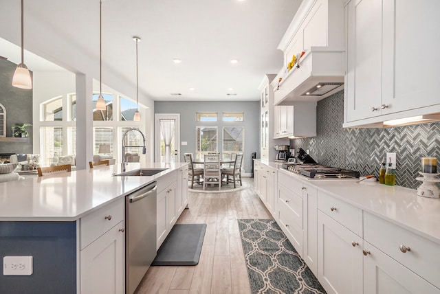 kitchen featuring appliances with stainless steel finishes, white cabinetry, light hardwood / wood-style flooring, sink, and decorative light fixtures