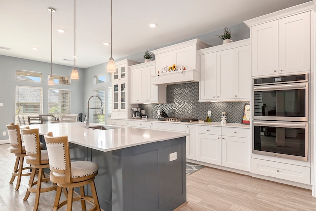 kitchen with appliances with stainless steel finishes, white cabinetry, hanging light fixtures, and light hardwood / wood-style floors